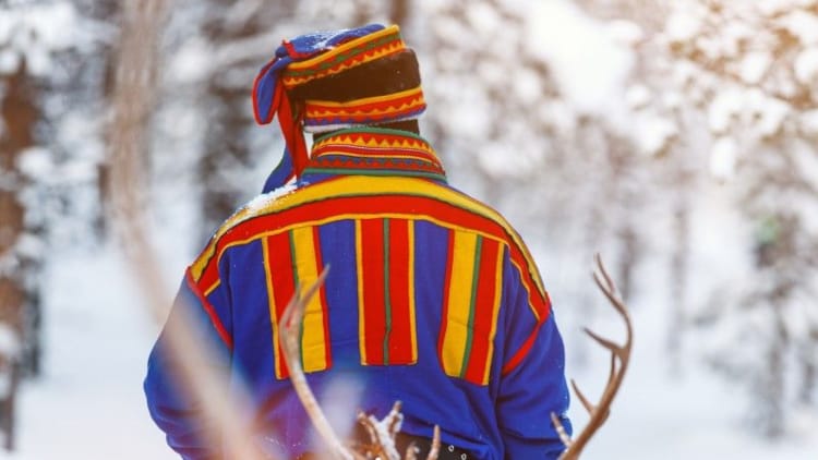 Mann med samisk antrekk fotografert bakfra i vintrelige omgivelser.