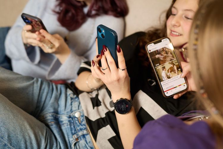 Tre tenåringsjenter i en sofa skroller på hver sin telefon.