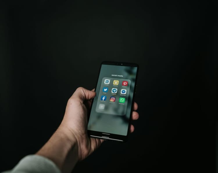 Hånd holder en smarttelefon med sosiale medier-appene synlige på skjermen.