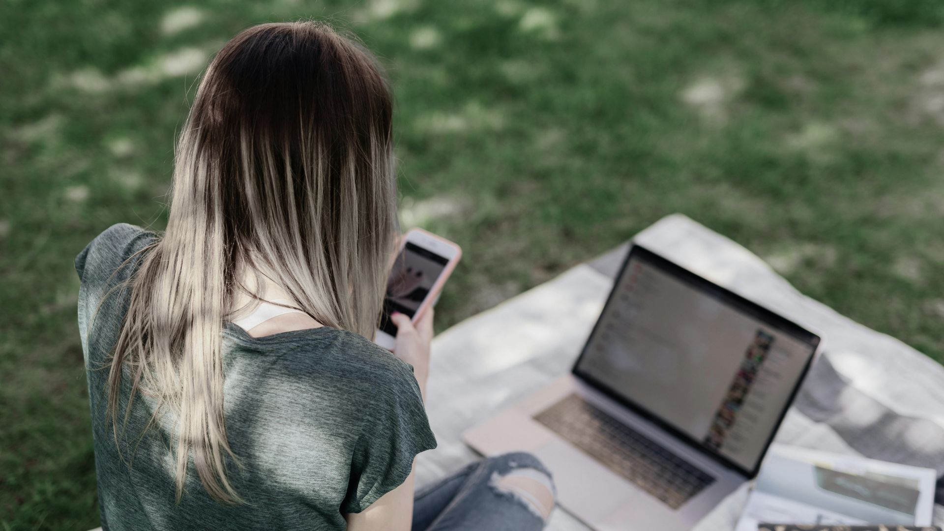 En jente sitter på gresset og ser på mobilen sin