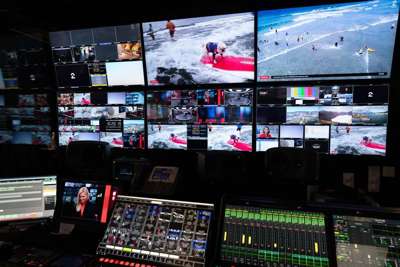 Kontrollpanel for tv-regi og mange skjermer med forskjellige bilder. Rommet er mørkt, men skjermene lyser opp.