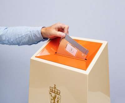 Øverste del av valgurne. En hånd er i ferd med å slippe en stemmeseddel ned i.