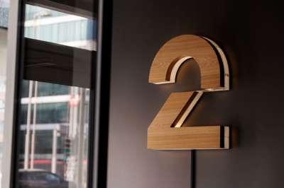 TV 2-logo på innendørs vegg. To-tallet i eik med opplyst bakgrunn mot mørkt malt vegg.