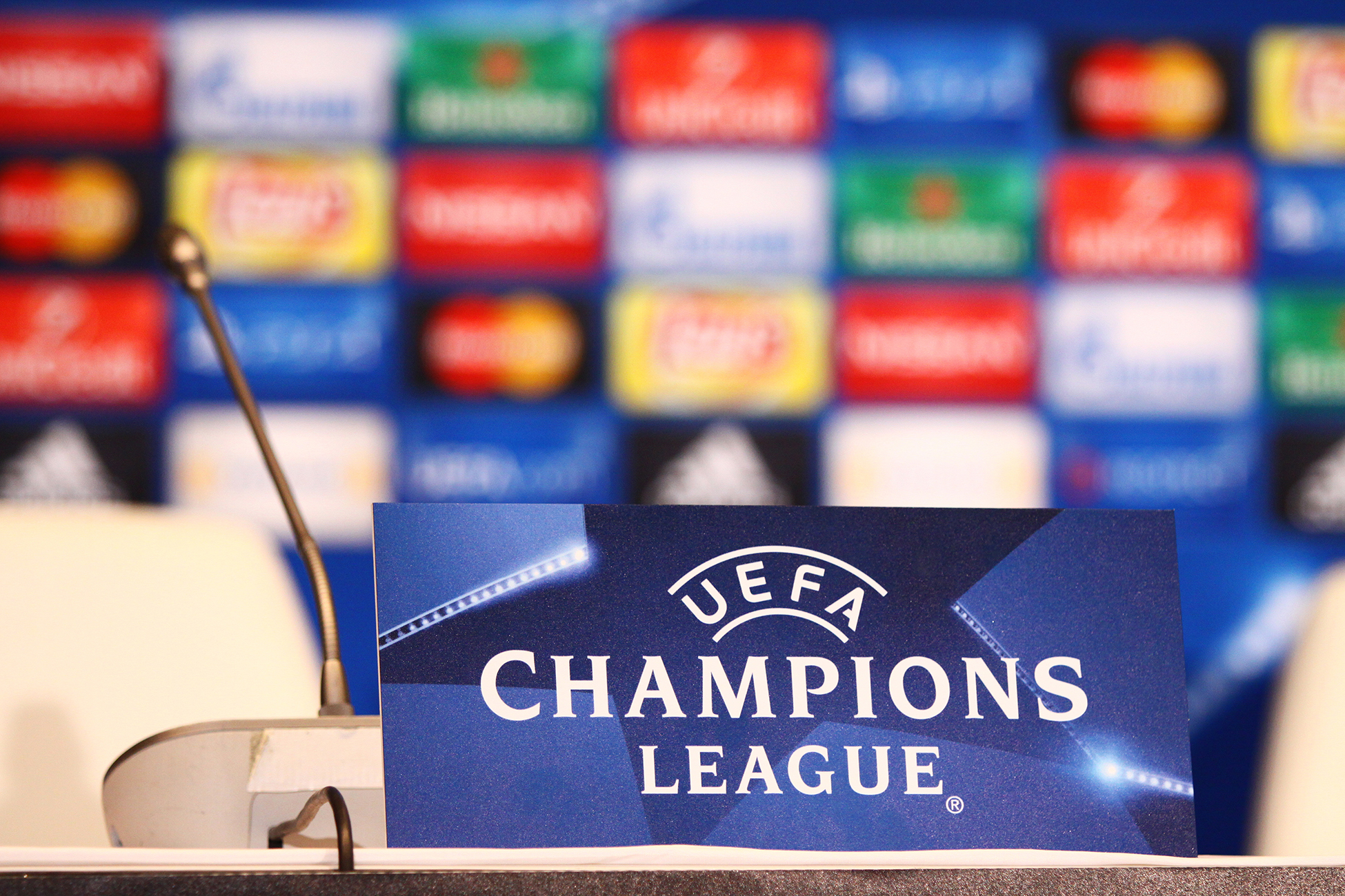 Podium med mikrofon foran et skilt med teksten &laquo;UEFA Champions League&raquo;. I bakgrunnen sees en uskarp vegg med fargerike sponsorlogoer, typisk fra en pressekonferanse i fotball.
