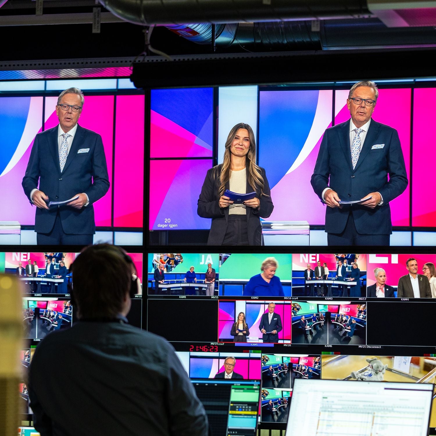 Kontrollrom under en TV-sending. Flere skjermer viser programledere og debattdeltakere i et fargerikt studio med rosa og bl&aring; grafikk. En person sitter foran monitorene og styrer sendingen fra kontrollpulten.