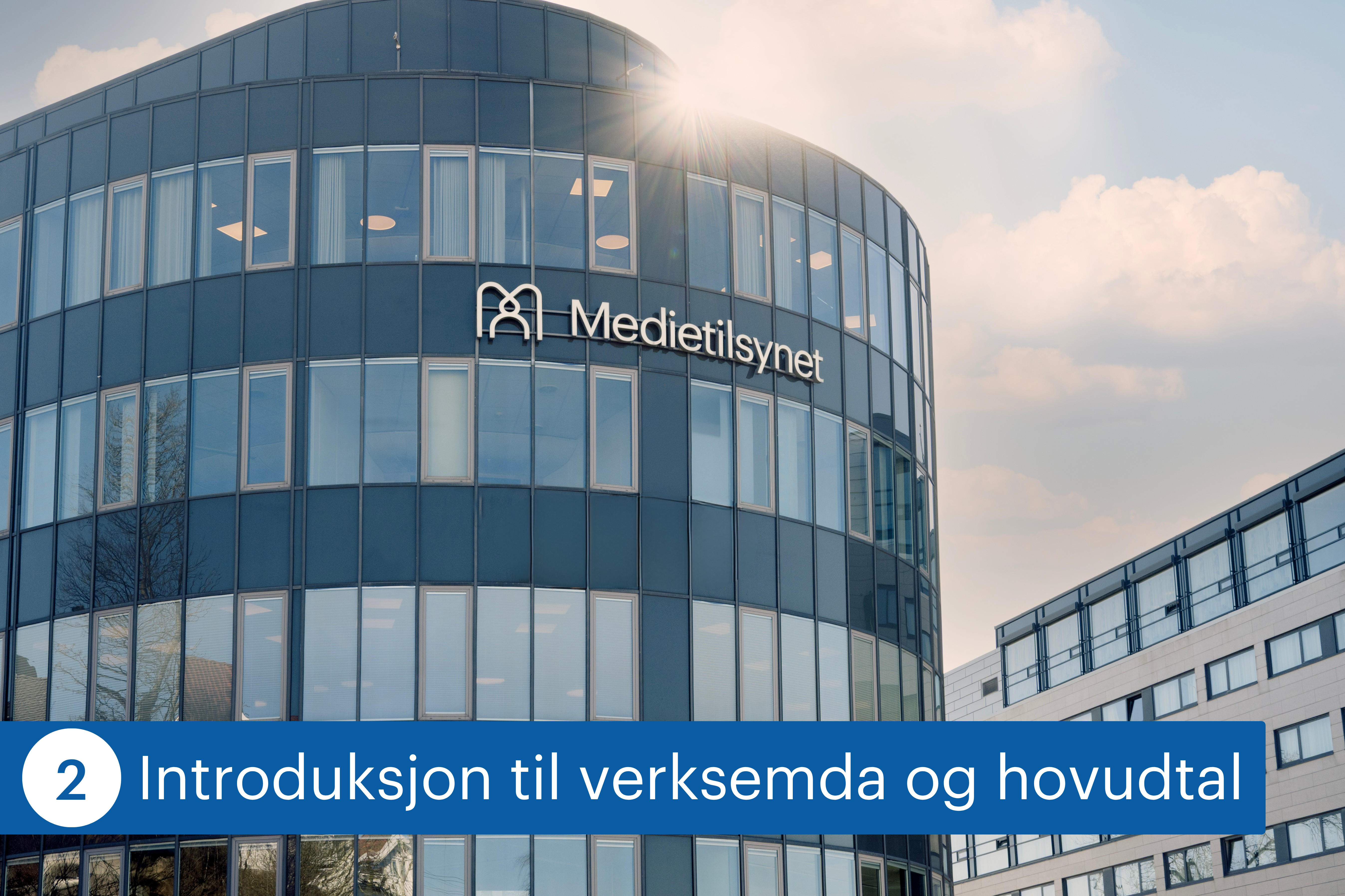 Moderne kontorbygg med buet glassfasade og skiltet &laquo;Medietilsynet&raquo; p&aring; utsiden. Sollys skinner over bygget, og et annet kontorbygg er synlig i bakgrunnen.