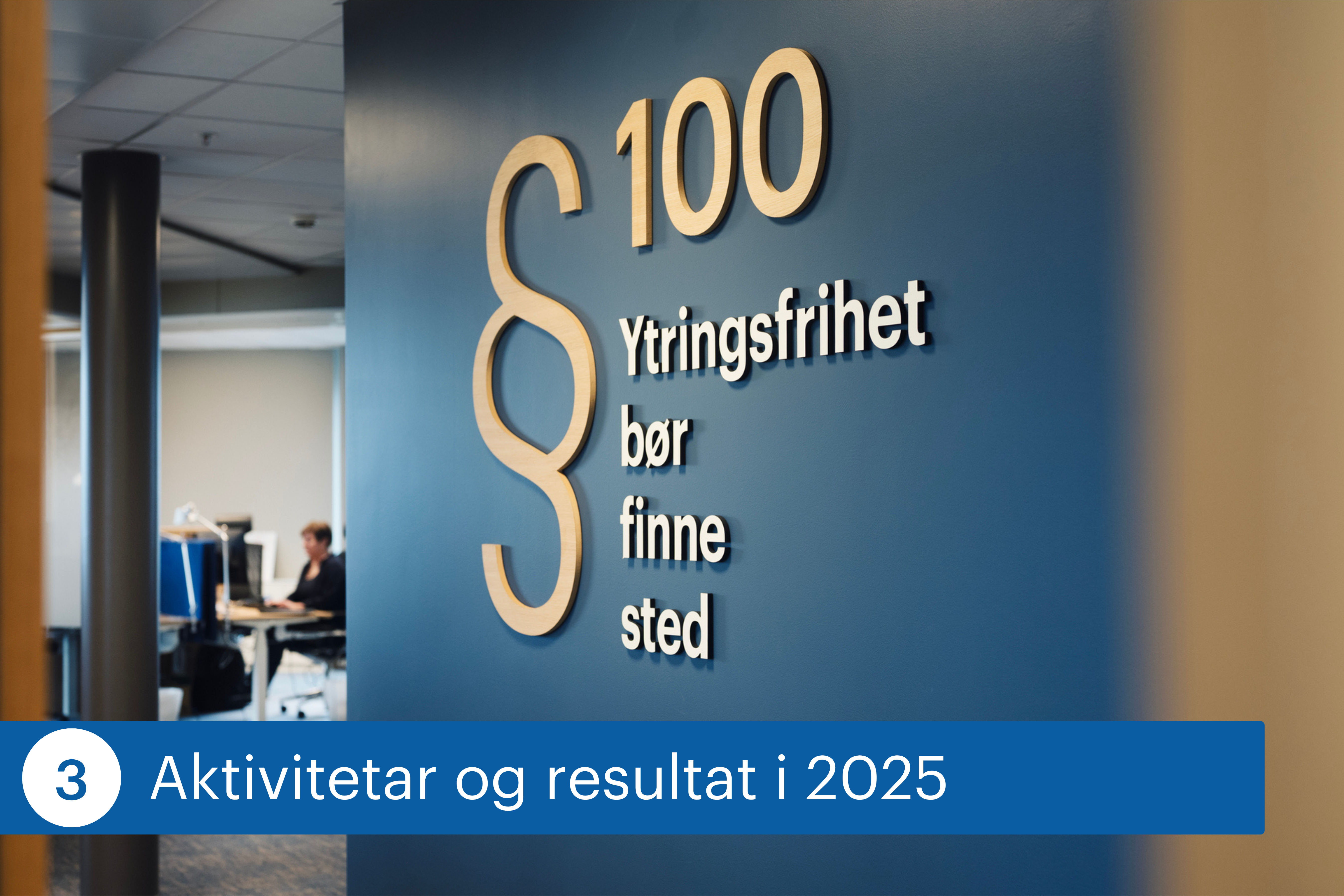 Vegg i kontorlokale med teksten &laquo;&sect; 100 Ytringsfrihet b&oslash;r finne sted&raquo;. I bakgrunnen sitter en person og jobber ved en pult i et &aring;pent kontoromr&aring;de.