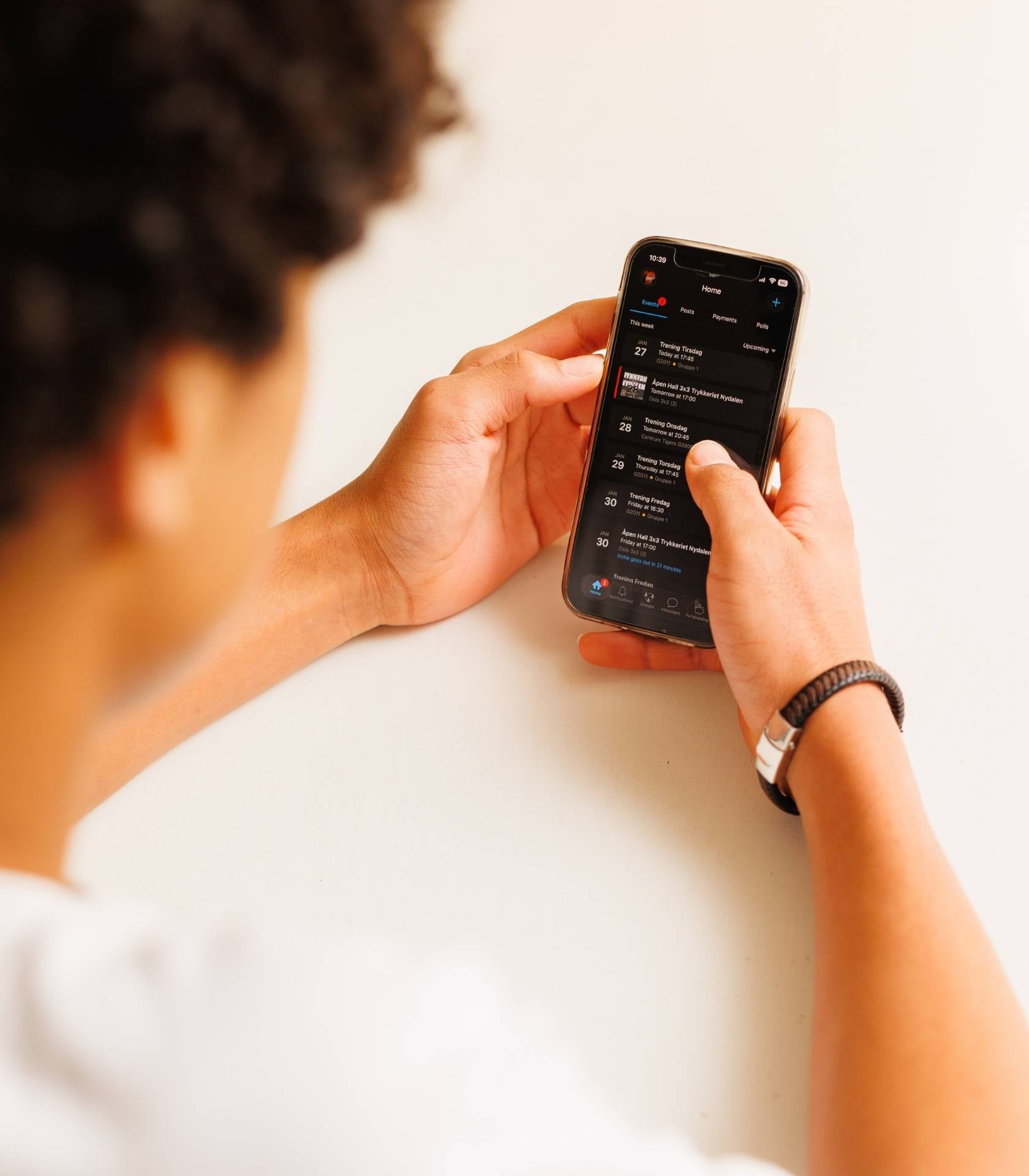 Ung person holder en mobiltelefon og ser p&aring; en oversikt over kommende aktiviteter og arrangementer i en app.
