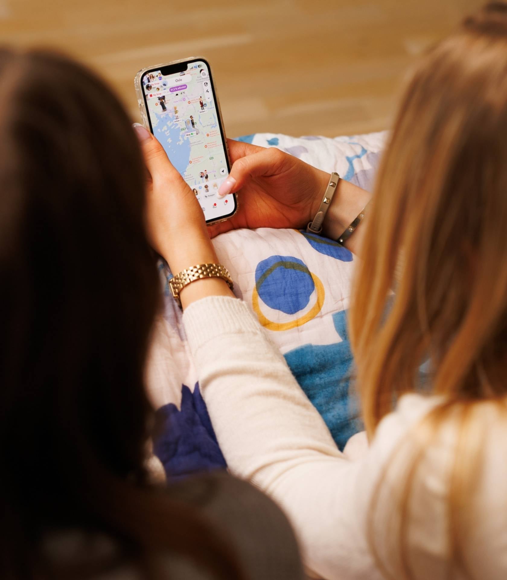 To unge sitter sammen og ser p&aring; en mobiltelefon som viser et digitalt kart med profiler og mark&oslash;rer.